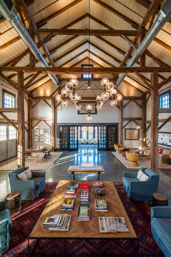 a beautiful barndominium space with wooden beams, exposed pipes and a statement chandelier plus muted touches of color