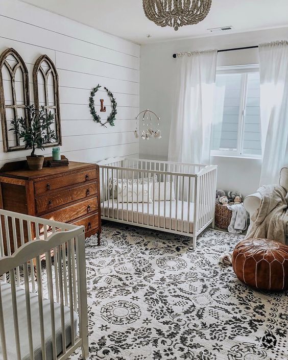 a farmhouse meets boho nursery with stained wooden furniture, a leather ottoman, a printed rug and greenery
