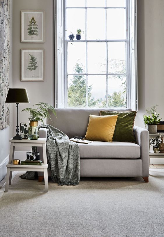 a neutral grey loveseat with colorful pillows and a printed blanket is an ideal piece for your cozy reading nook