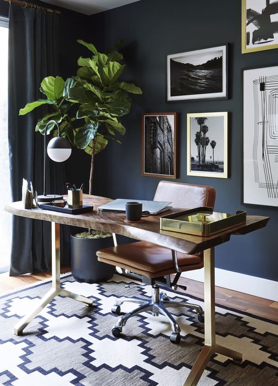 navy walls, curtains and pots set the tone of the home office, and a wooden desk and leather chair soften it