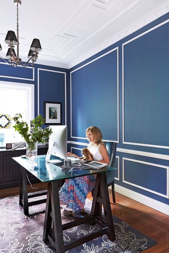 an elegant home office with navy and white walls, a dark blue patterned rug and a catchy trestle desk with a glass top
