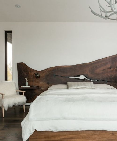 a modern bedroom with a rich stained live edge wooden headboard, an antler chandelier and a faux fur chair