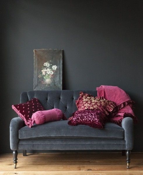 a super elegant black velvet loveseat with refined legs and fuchsia and purple pillows for a moody space