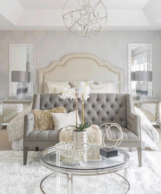 a super elegant grey tufted loveseat with a tall bench to create a sitting space at the bed