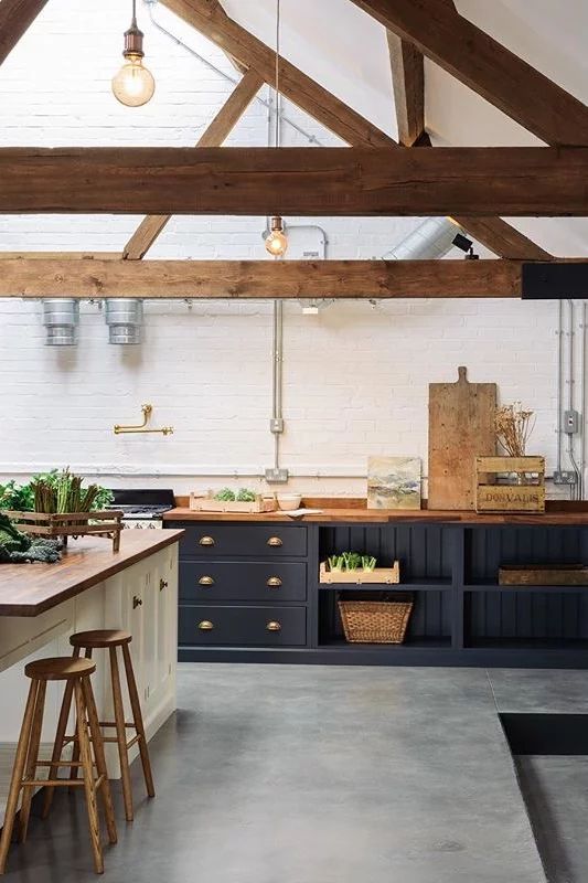 a chic barndominium kitchen with navy and white cabinets and wooden countertops and beams