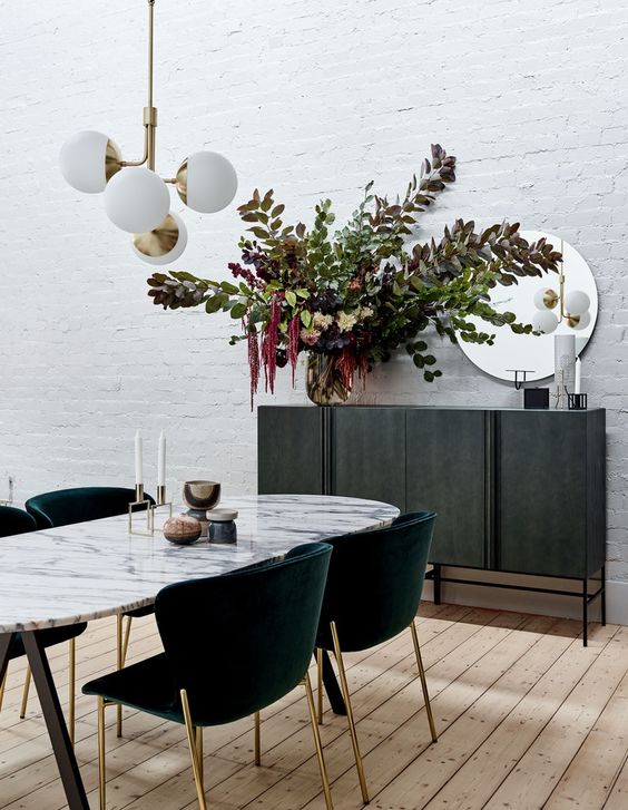 an oval dining table with a marble tabletop and dark green chairs with gold legs make the room very elegant