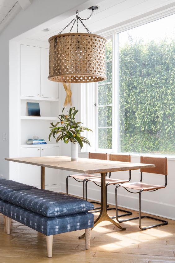A sleek wooden dining table, wooden chairs and an upholstered blue bench for a mid century modern space