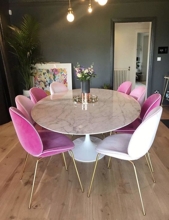 a glam dining space with a round marble dining table and white and pink velvet chairs