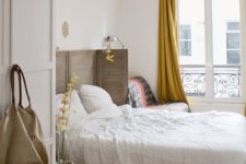 a Paris-inspired chic bedroom with a shutter screen as a headboard, a herringbone floor, mustard curtains and a comfy chair