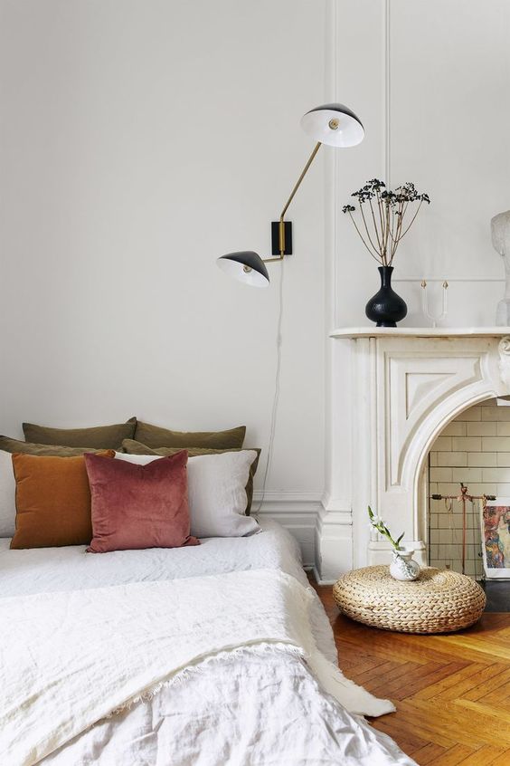 a beautiful Parisian bedroom with a faux fireplace, art deco lamps, a bed with muted pillows