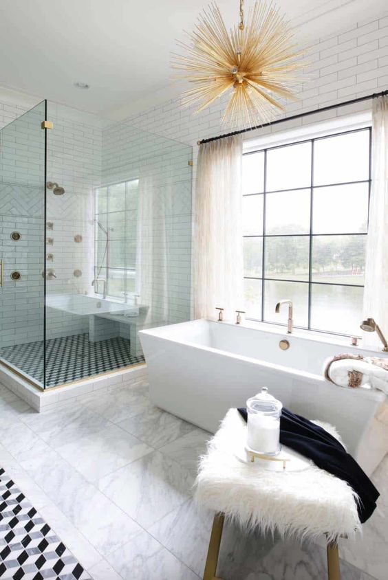 a beautiful transitional space with a catchy tub, a sunburst chandelier, a faux fur stool and mosaic tiles
