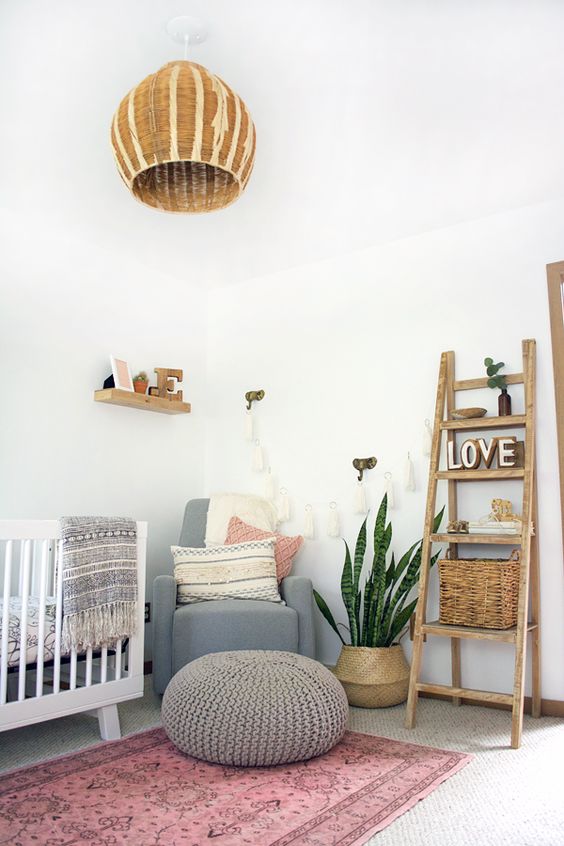 a boho chic nursery with a pink rug, touches of grey, a wicker lamp, a ladder with baskets