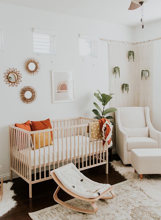 a boho chic nursery with potted greenery, a wooden crib and little rocker, a gallery wall and some boho rugs