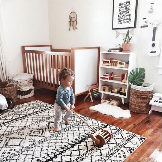 a boho nursery with a pritned rug, baskets, a dream catcher on the wall and some simple stuff