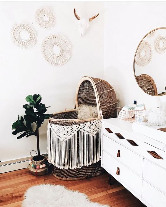 a boho nursery with a wicker bassinet with macrame, a white sideboard with leather touches and a gallery wall of macrame