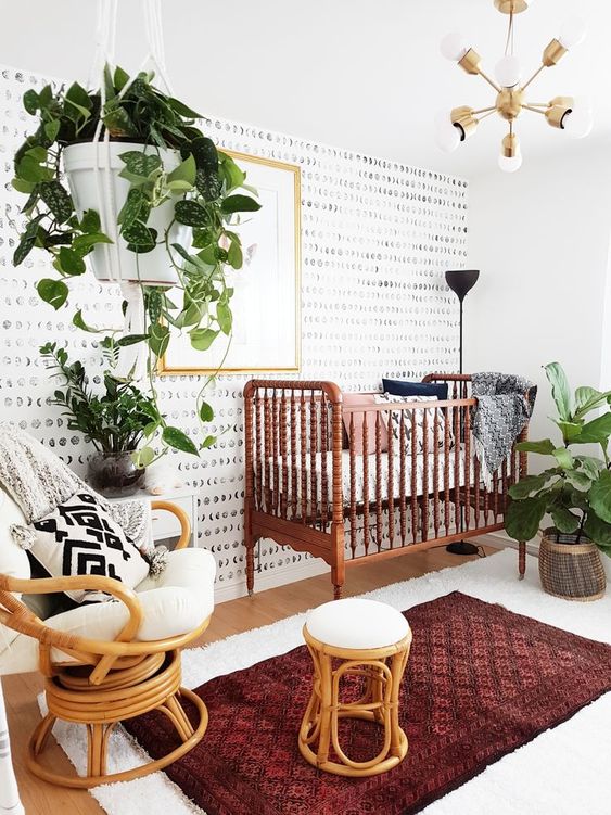 a bright modern boho nursery with a vintage crib, rattan chairs, boho rugs, potted greenery and an elegant chandelier