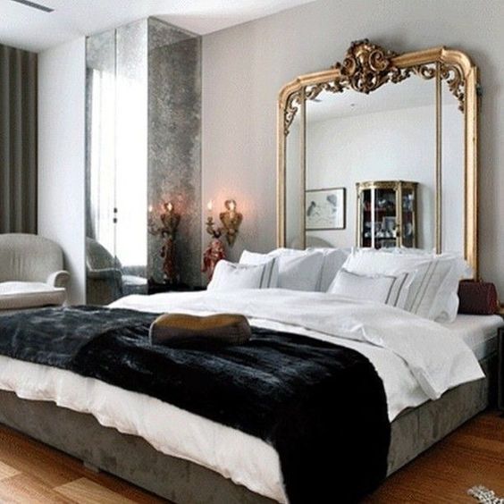 a chic Parisian space with a statement mirror headboard, a large bed, mirror panels and an antique lamp