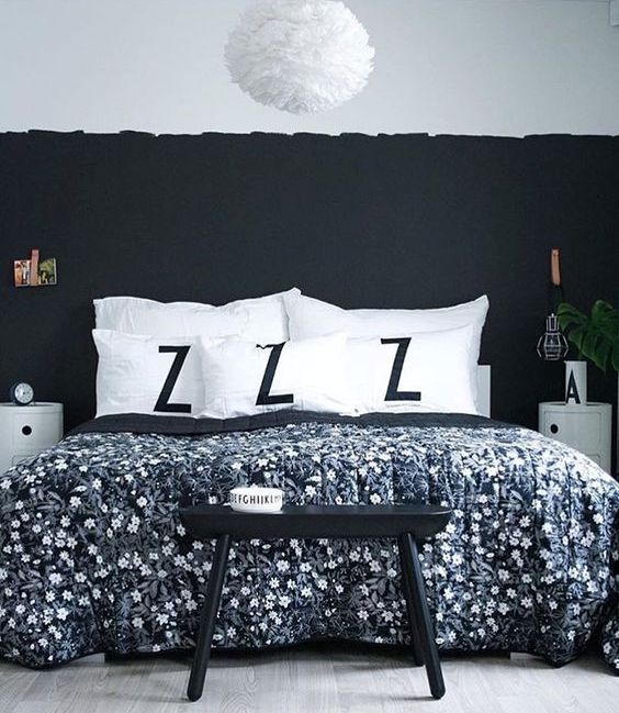 a chic bedroom with a black accent wall, a black stool, rounded nightstands and a fluffy lamp