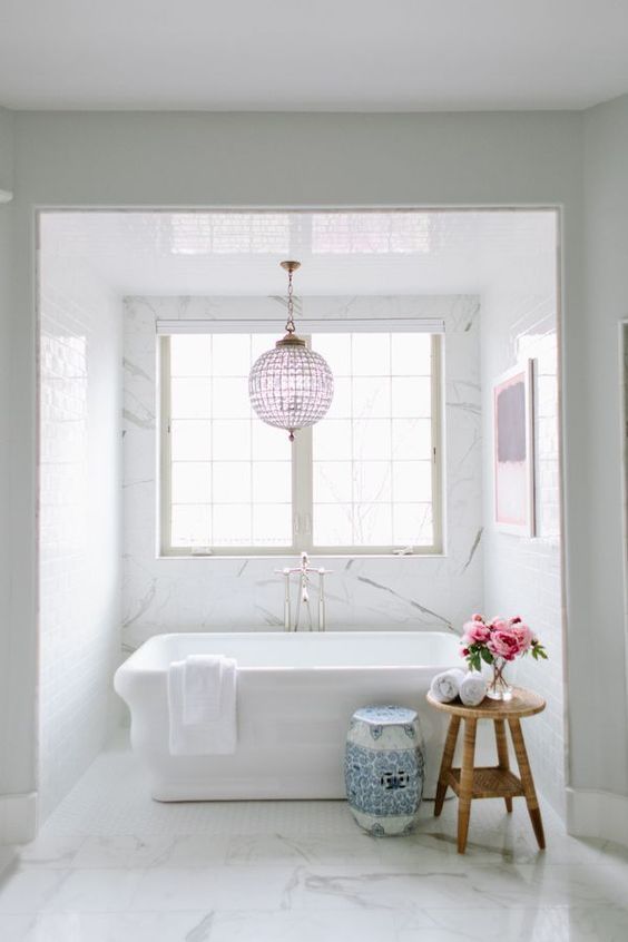 a chic transitional space with a lavender chandelier and artwork, an amazing blue porcelain stool and a chic tub