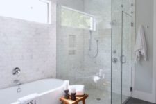 a chic transitional space with marble and grey tiles, a contemporary oval tub, a wooden stool and a seamless shower