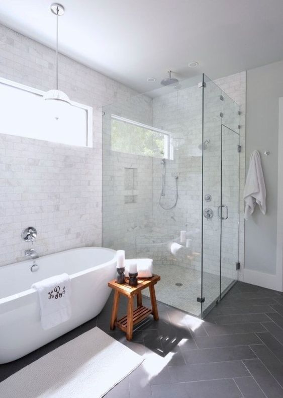 a chic transitional space with marble and grey tiles, a contemporary oval tub, a wooden stool and a seamless shower