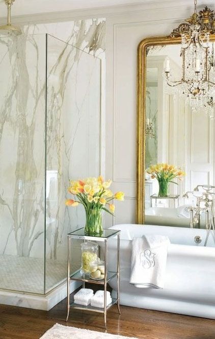 a chic vintage bathroom with white stone tiles, paneling, a sstatement mirror and a crystal chandelier
