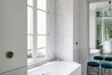 a contemporary Parisian bathroom done with white marble, chevron clad floor, teal stools and cabinets on the walls