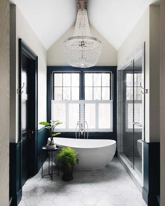 a contemporary Parisian bathroom with an oval tub, a large crystal chandelier, black and white walls and a hex tile floor