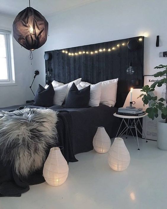 a contemporary boho bedroom with a black rustic bed, mismatching nightstands, a black lamp and white candle lanterns