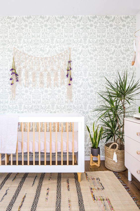 a cute boho nursery with a botanical wallpaper wall, a boho rug, a crib, macrame and potted greenery