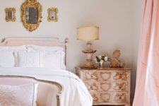 a dreamy Parisian bedroom done in neutrals and blush, with an arrangement of mirrors, refined vintage furniture with gold inlays