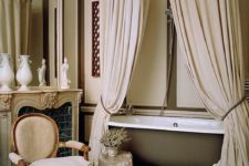 a fantastic neutral vintage-inspired Parisian bathroom with canopies, a bathtub, a vintage chair and a faux fireplace