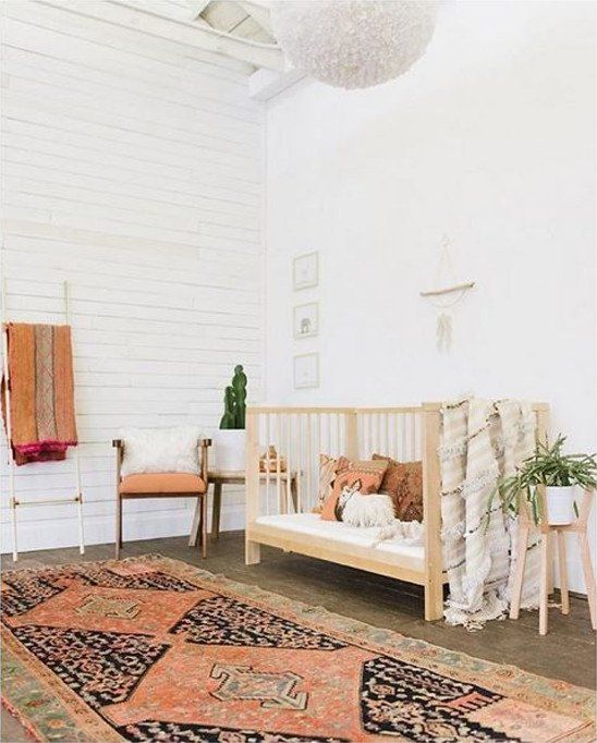 A free spirited nursery with a boho rug, a wooden crib, potted greenery and touches of faux fur here and there