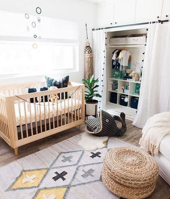 a fun boho nursery with a printed rug, a jute ottoman, a wooden crib, an oversized tassel and a large fun wicker whale for storage
