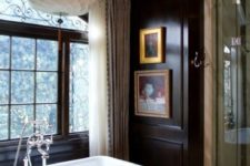 a gorgeous vintage bathroom with black walls, a vintage tub, a gorgeous chandelier and artworks
