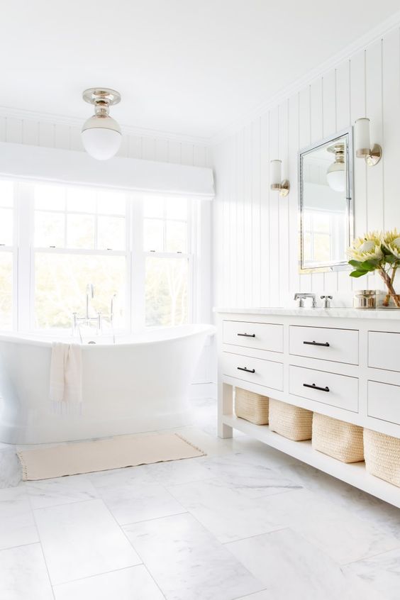 a light-filled transitional white bathroom with a traditional white vanity, a vintage tub and a pendant lamp plus marble tiles