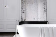 a minimalist Parisian bathroom with a tub on a stone platform, a vintage mirror, stucco walls and catchy minimal lamps