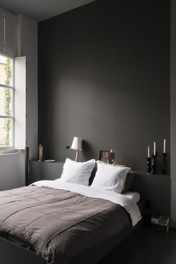 A minimalist bedroom with a black statement wall, a shelf, a built in bed and white lamps