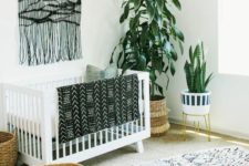 a monochromatic boho nursery with a black macrame hanging, a printed rug, a folksy print blanket and potted plants