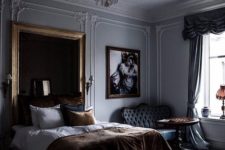 a moody refined bedroom with a statement chandelier, artworks, stucoo, a dark upholstered headboard and sophisticated furniture