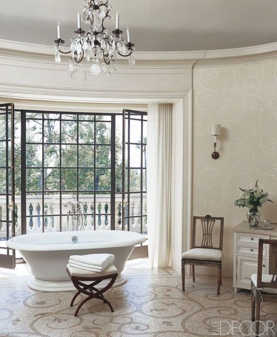 a neutral Parisian bathroom with a crystal chandelier, a chic vintage bathtub, a patterned floor and elegant furniture