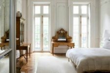 a neutral Parisian bedroom with antique wooden furniture, a crystal chandelier and large windows to fill the space with light