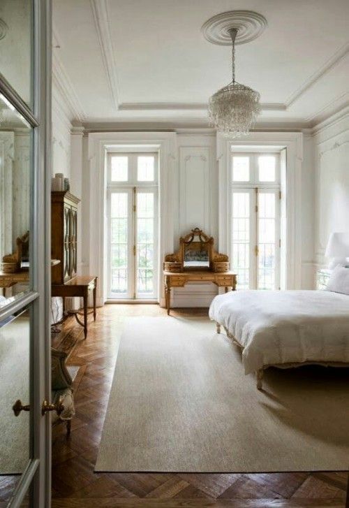 a neutral Parisian bedroom with antique wooden furniture, a crystal chandelier and large windows to fill the space with light