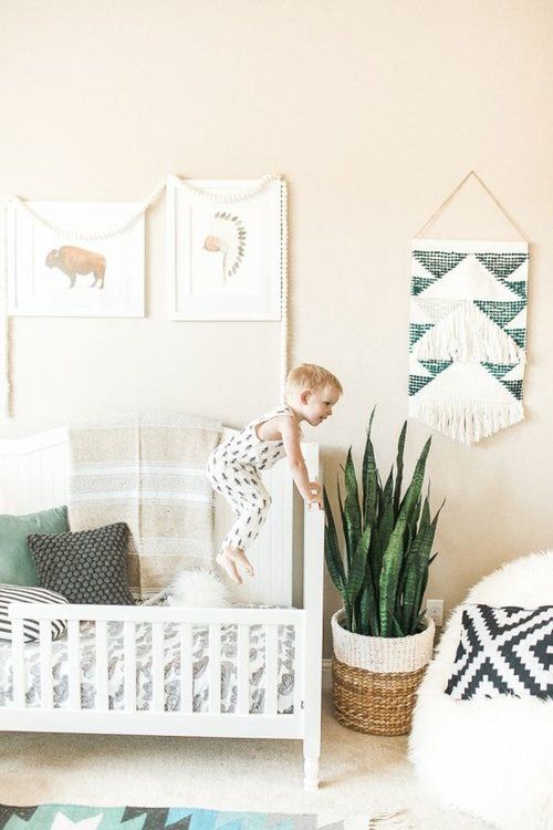 a neutral boho nursery with a woven sign, a gallery wall, a basket planter and a large fluffy pouf