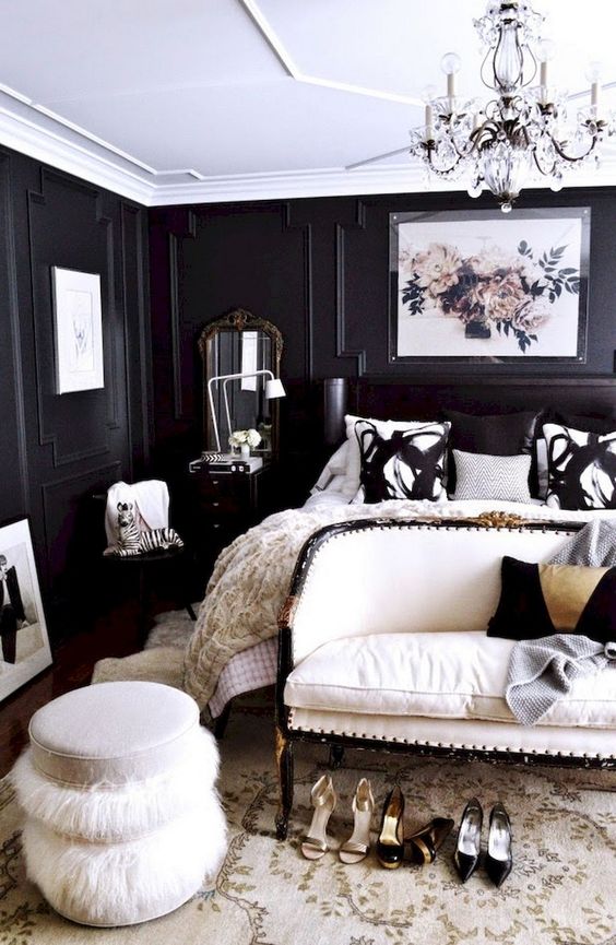 a refined and luxurious black and white bedroom with paneled walls, a black bed, a white upholstered loveseat and a fluffy ottoman