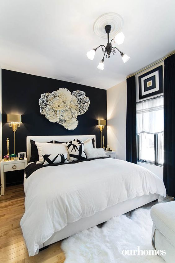 a refined black and white bedroom with a statement wlal, a flower-inspired installation, a white bed and gorgeous wall lamps
