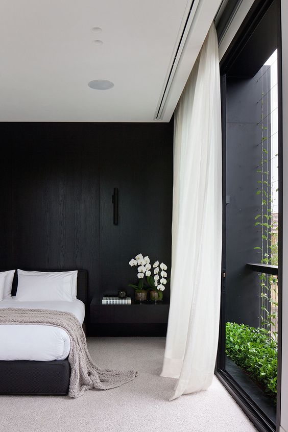 a refined minimalist black and white bedroom with a statement wall, a black bed, white curtains and stylish bedding