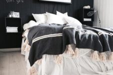 a stylish black and white bedroom with a black accent wall, black floating nightstands, chic bedding and a blanket with tassels