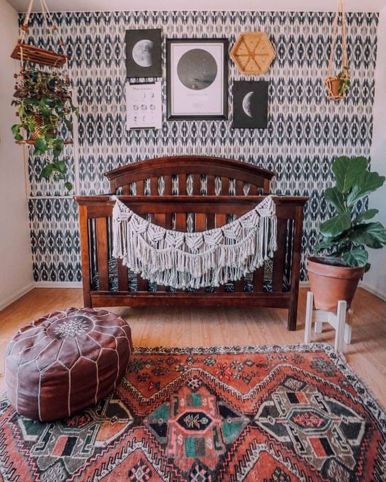 a stylish boho nursery with a monochromatic printed wall, a gallery wall, potted greenery, a boho rug and a leather ottoman