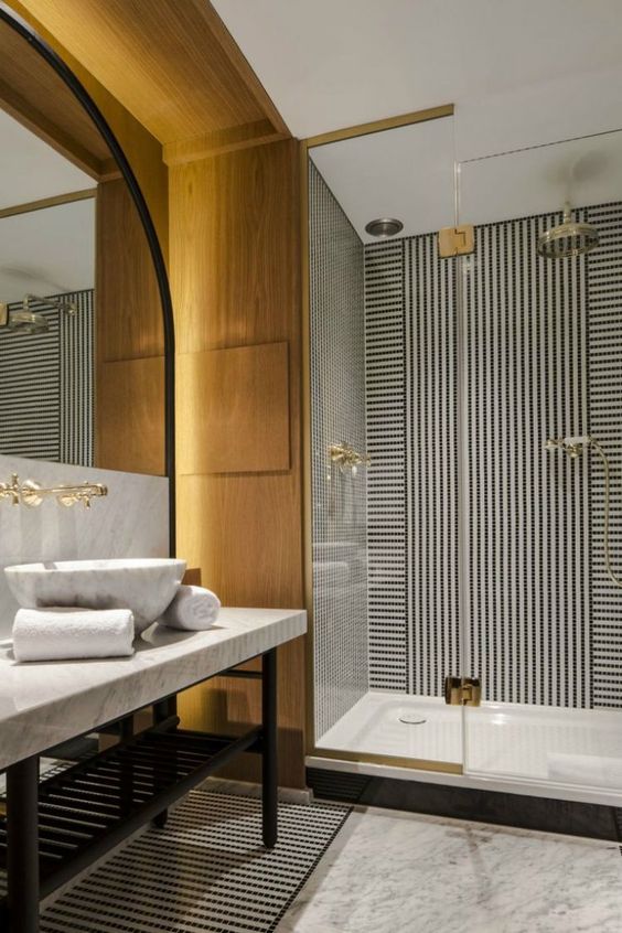 a stylish contemporary bathroom in black and white and with light-colored wood, gilded touches and a statement mirror